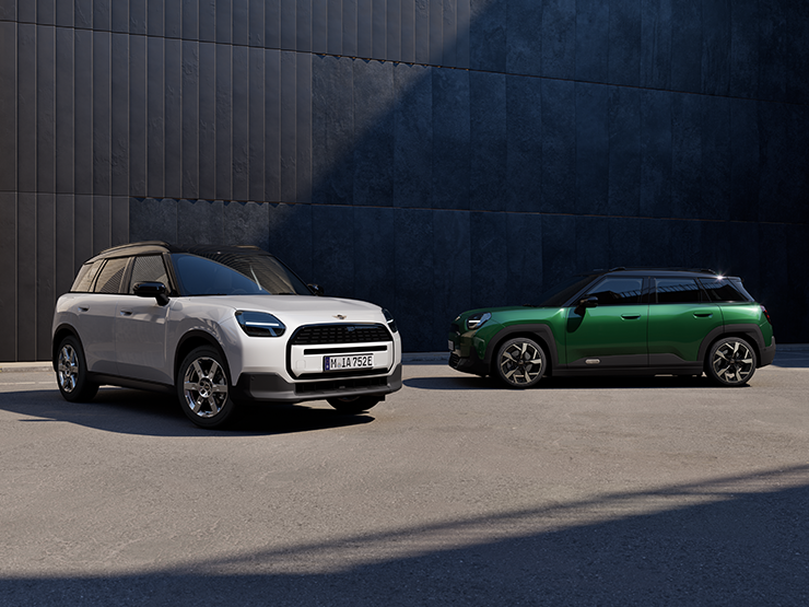 Sen fuldelektriske MINI Aceman i Nanuq White og British Racing Green med sort tag set forfra og fra siden på en gade.