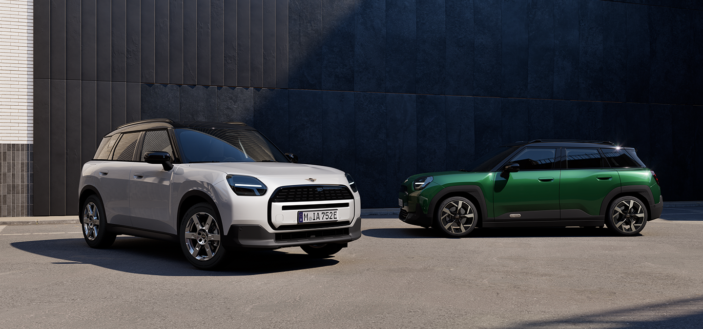 Sen fuldelektriske MINI Aceman i Nanuq White og British Racing Green med sort tag set forfra og fra siden på en gade.