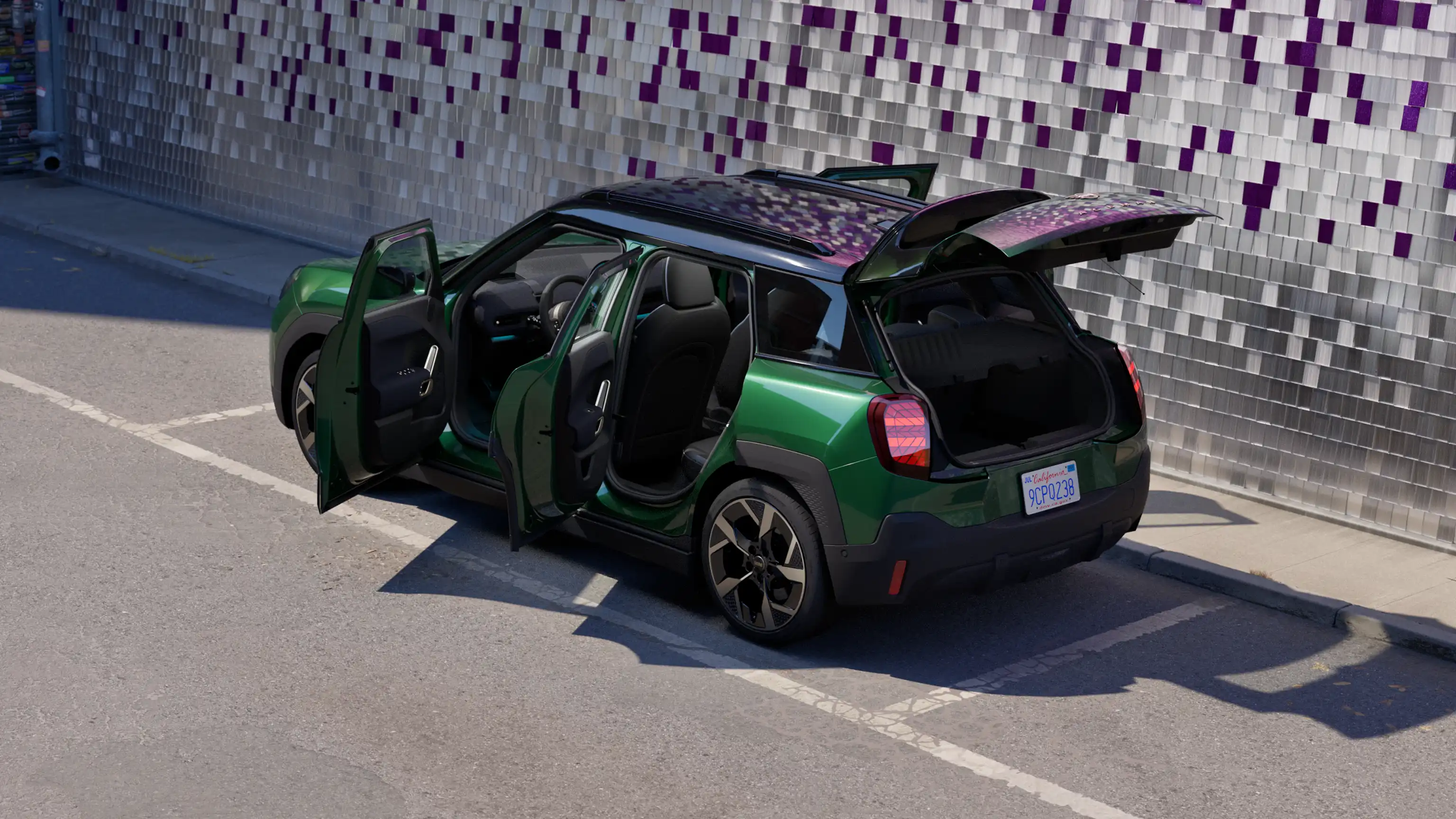 Sidevisning af bagsiden på en parkeret, fuldelektrisk MINI Aceman i British Racing Green på en parkeringsplads med alle døre åbne og en farverig væg i baggrunden
