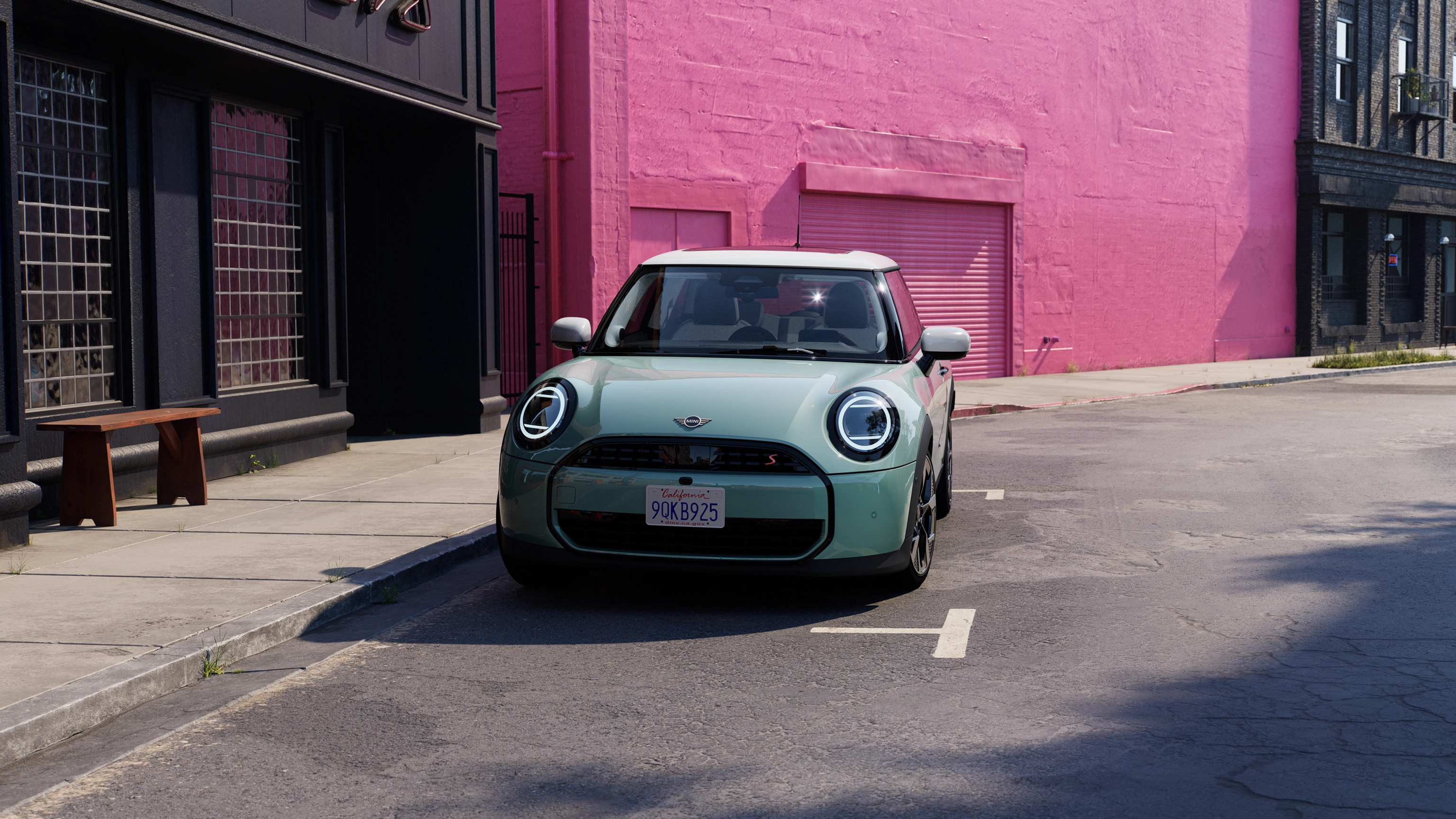 En parkeret MINI Cooper i Ocean Wave Green med hvidt tag set forfra på en gade med en lyserød mur i baggrunden