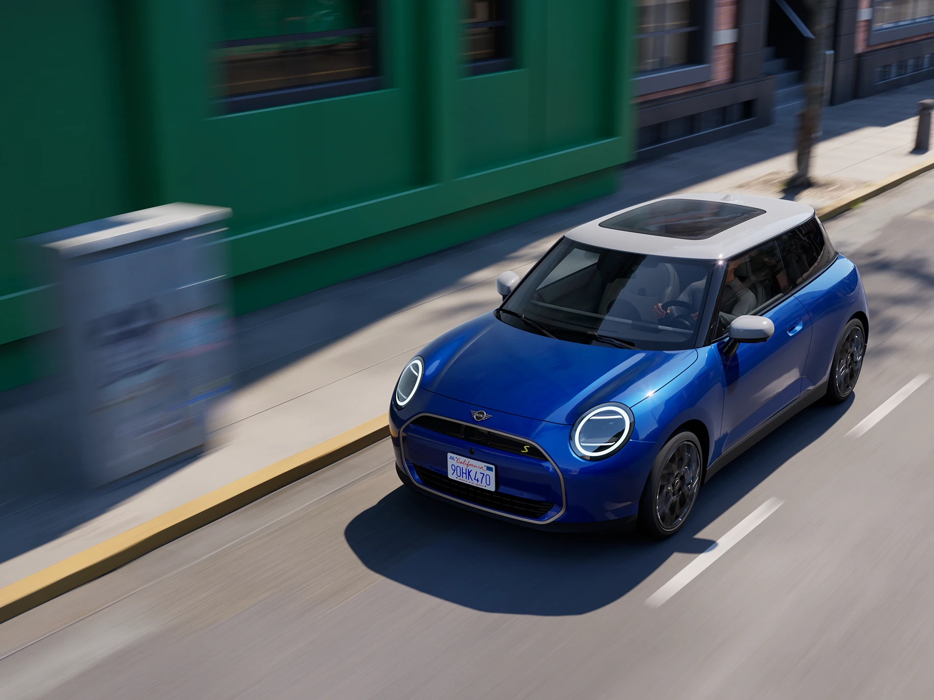 Den fuldelektriske MINI Cooper i Blazing Blue med hvidt tag kørende på en gade. 