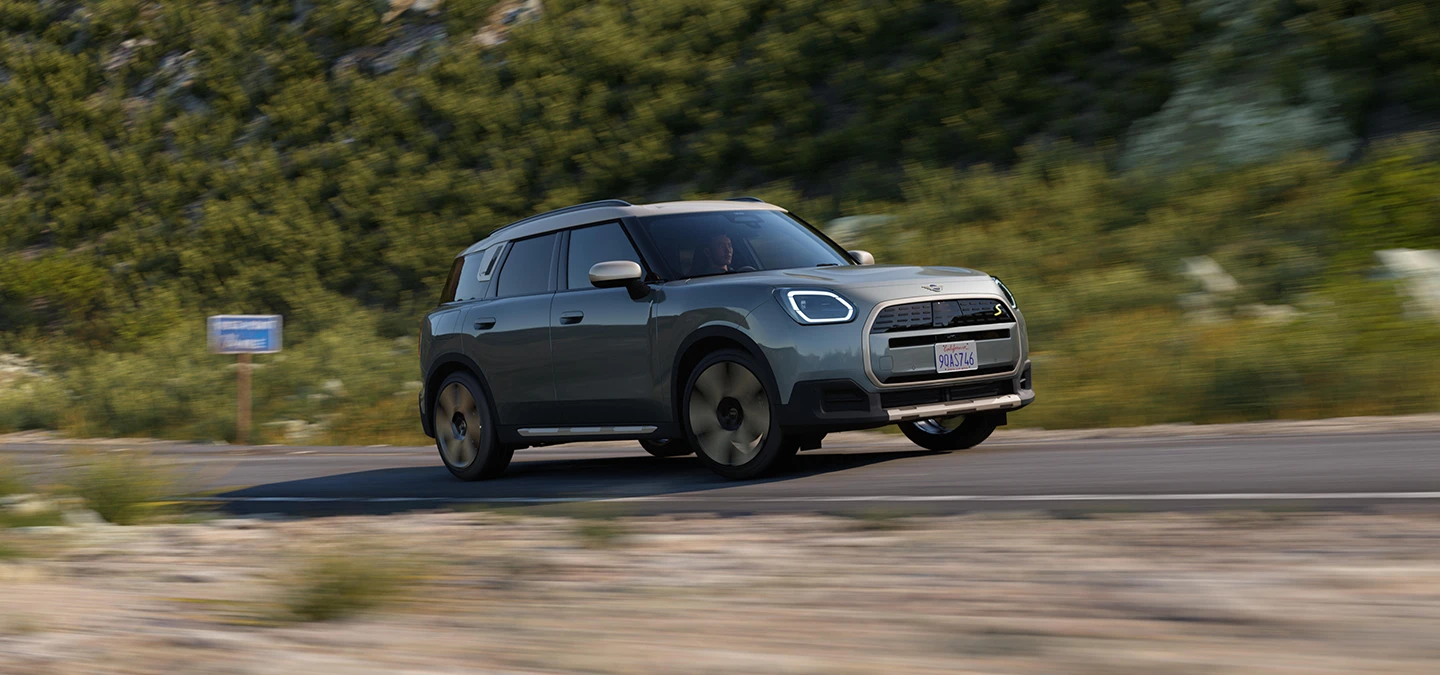 En fuldelektrisk kørende MINI Countryman i Smokey Green med tag i Vibrant Silver set fra siden.