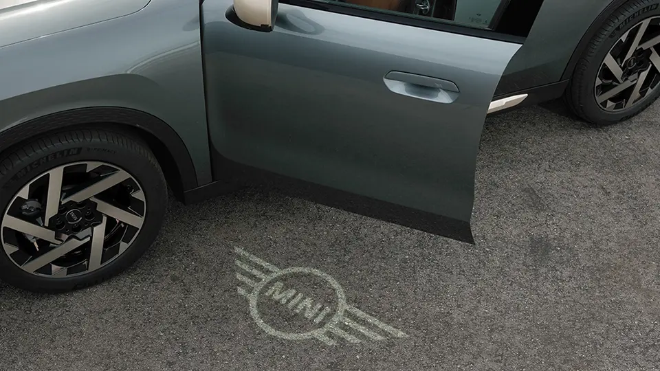 MINI Countryman set udefra med åben dør og MINI-logoets velkomstlys på jorden 