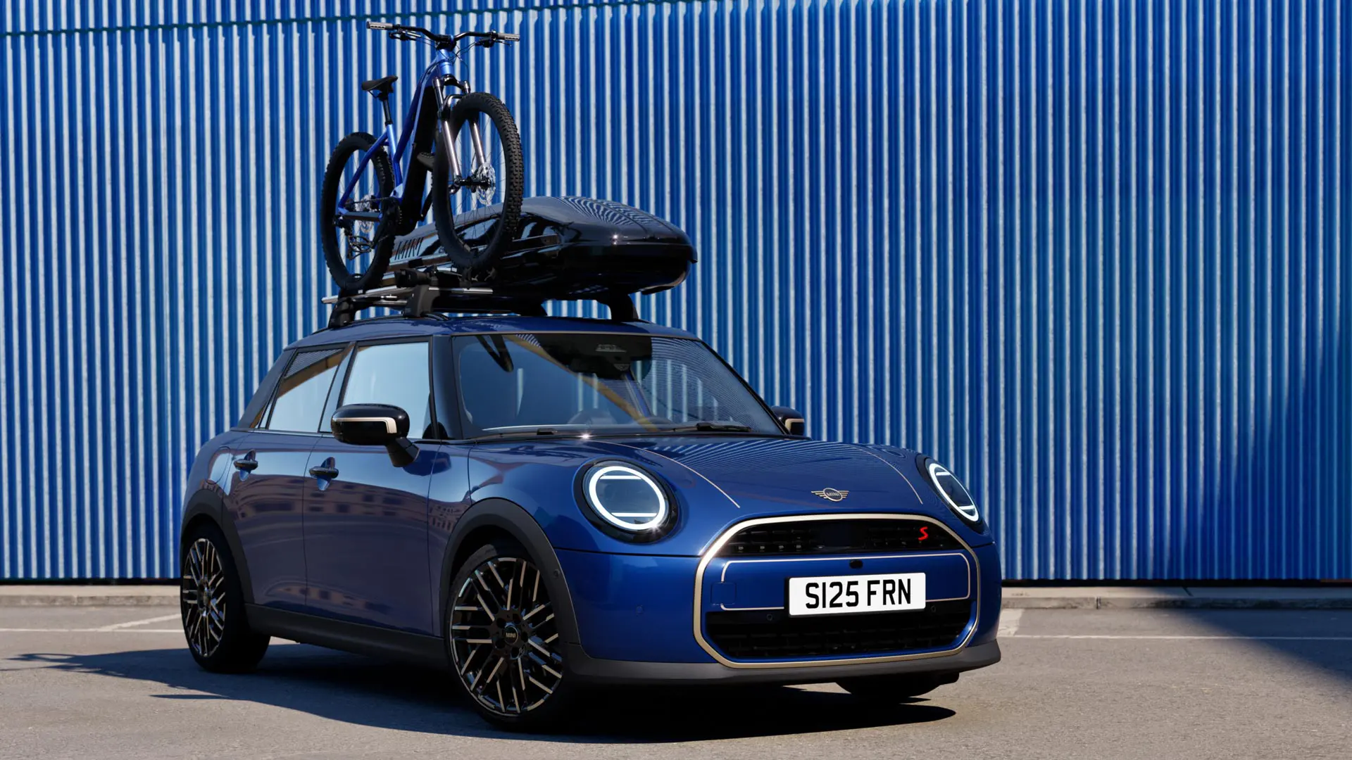 MINI Aceman i Indigo Sunset Blue set forfra med MINI Tagcykelholder med en mountainbike og MINI Tagboks 320.