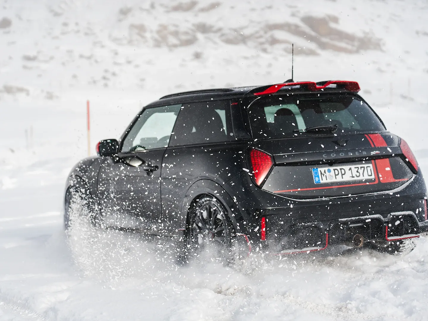 Visning bagfra af en MINI Cooper JCW, der kører gennem sneen.