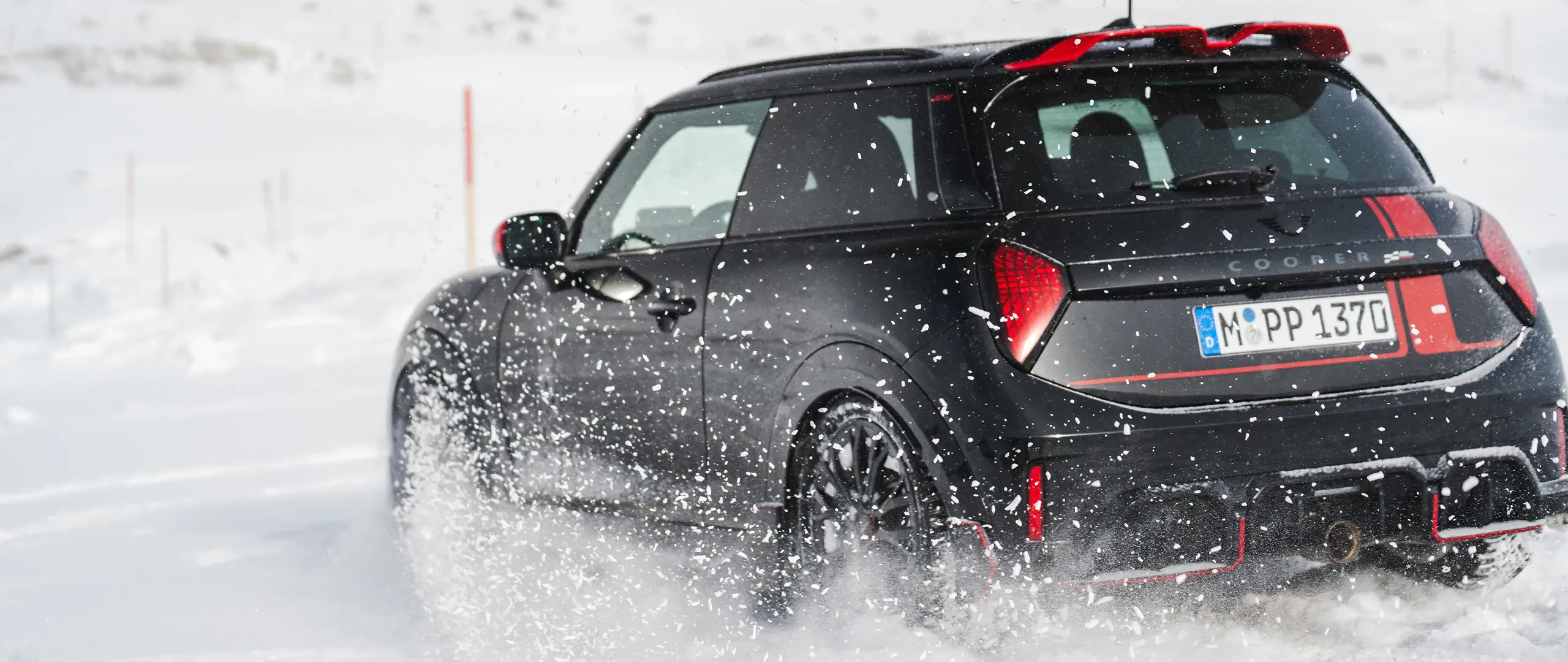 Visning bagfra af en MINI Cooper JCW, der kører gennem sneen.