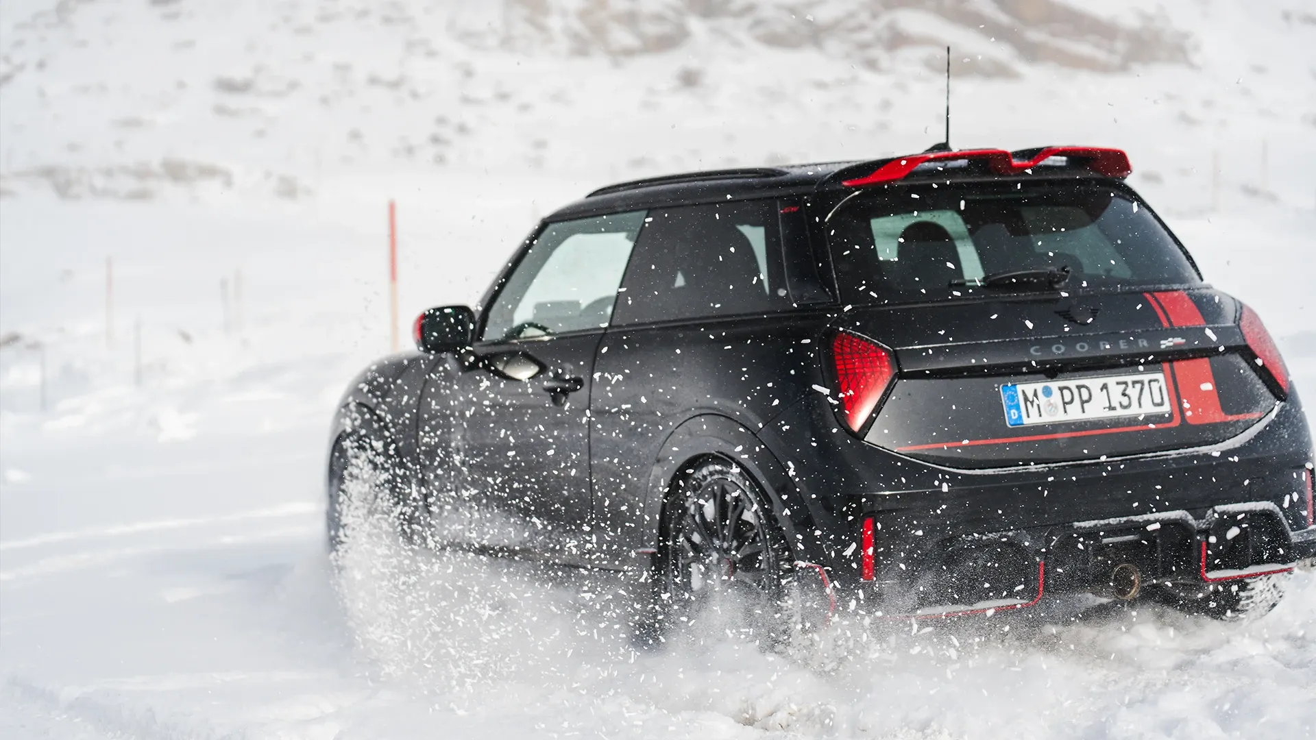 Visning bagfra af en MINI Cooper JCW, der kører gennem sneen.