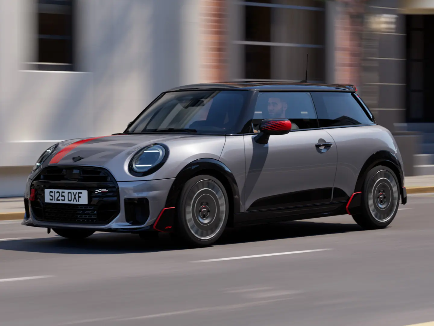 MINI Cooper 3-dørs i Melting Silver med John Cooper Works spejlkapper og fartstriber på motorhjelmen i Chili Red, tagspoiler og winglet i sort, kørende gennem byens gader – set skråt forfra.